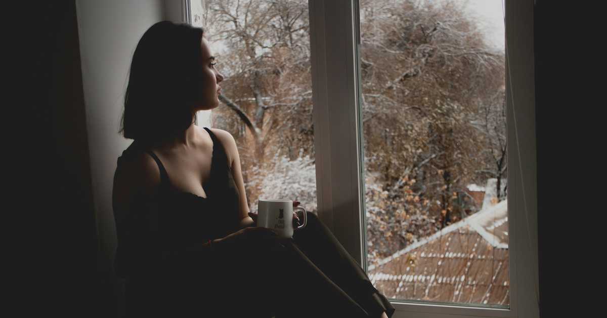 Femme qui regarde par la fenêtre en tenant un mug sur ses genoux